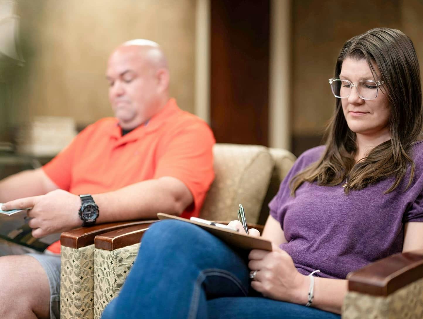 Woman in purple writing in clipboard sitting in waiting room