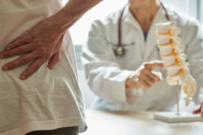 doctor showing patient the anatomy of the spine while patient is holding his own back in pain
