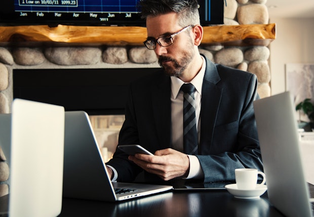 man in a suit with a laptop in front of him and phone in hand