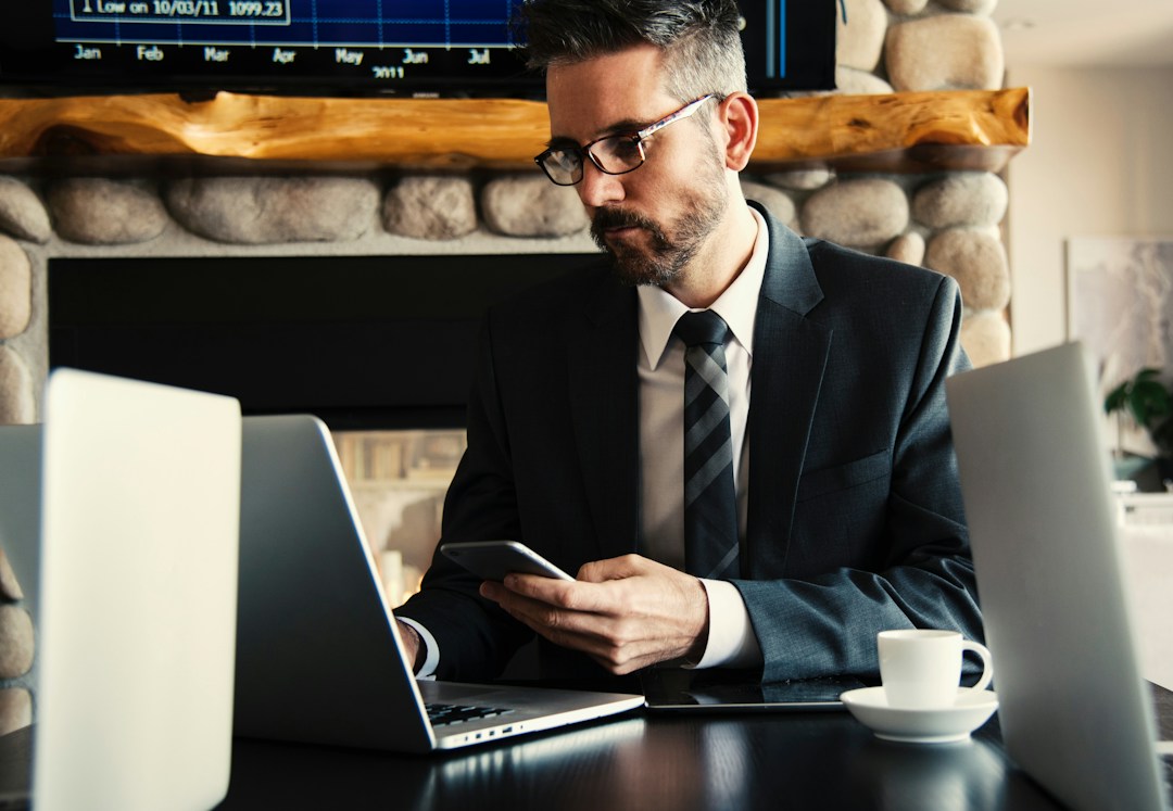 man in a suit with a laptop in front of him and phone in hand