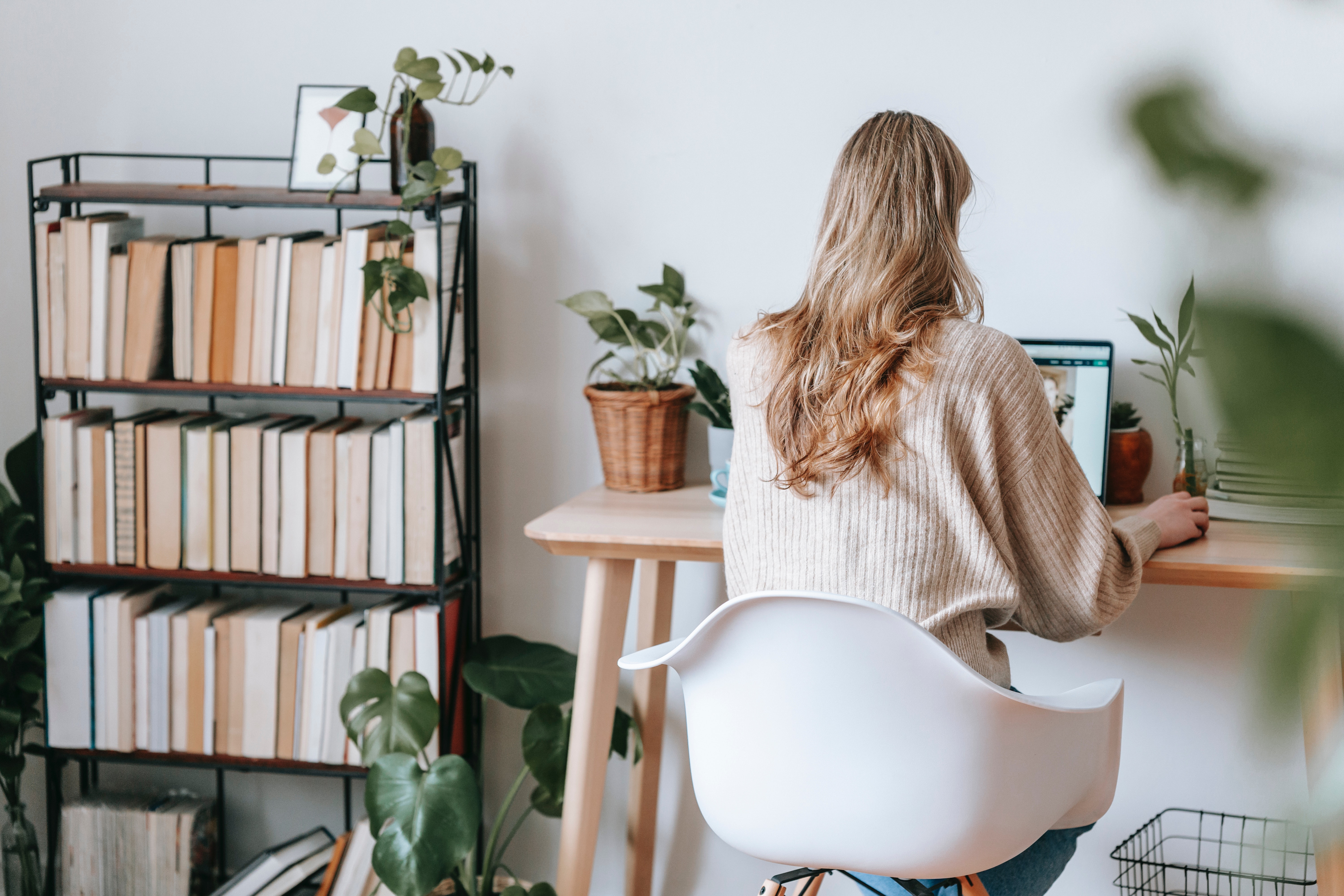 blonde woman typing at a desk with a bookshelf to her left and plants