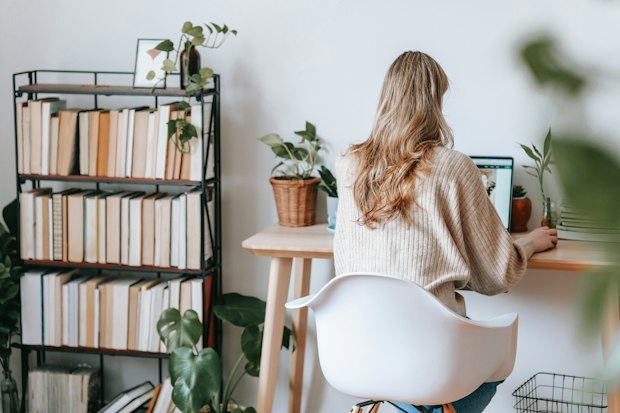 blonde woman typing at a desk with a bookshelf to her left and plants
