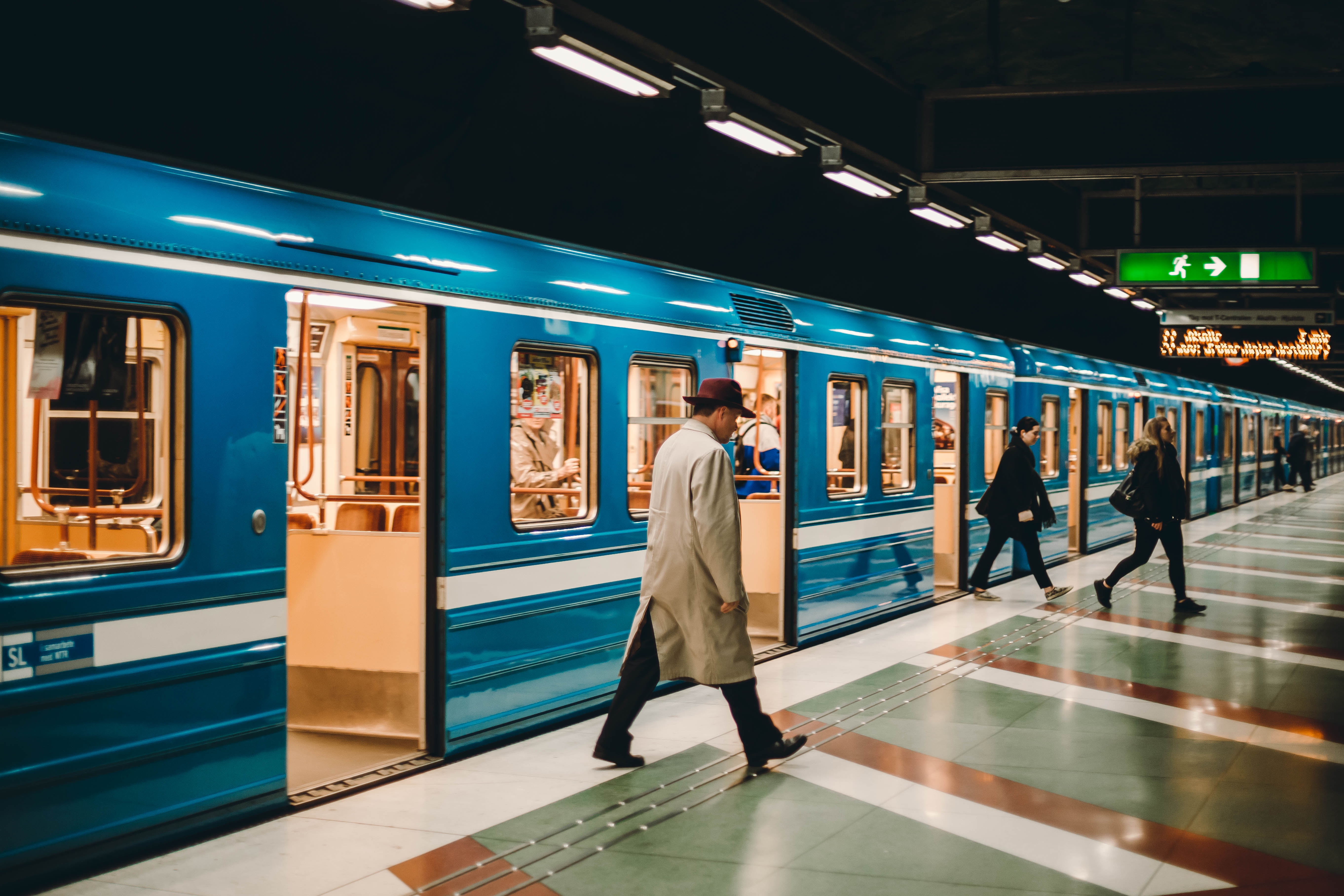 a blue train with the doors open as a man along the platform in a long jacket and at