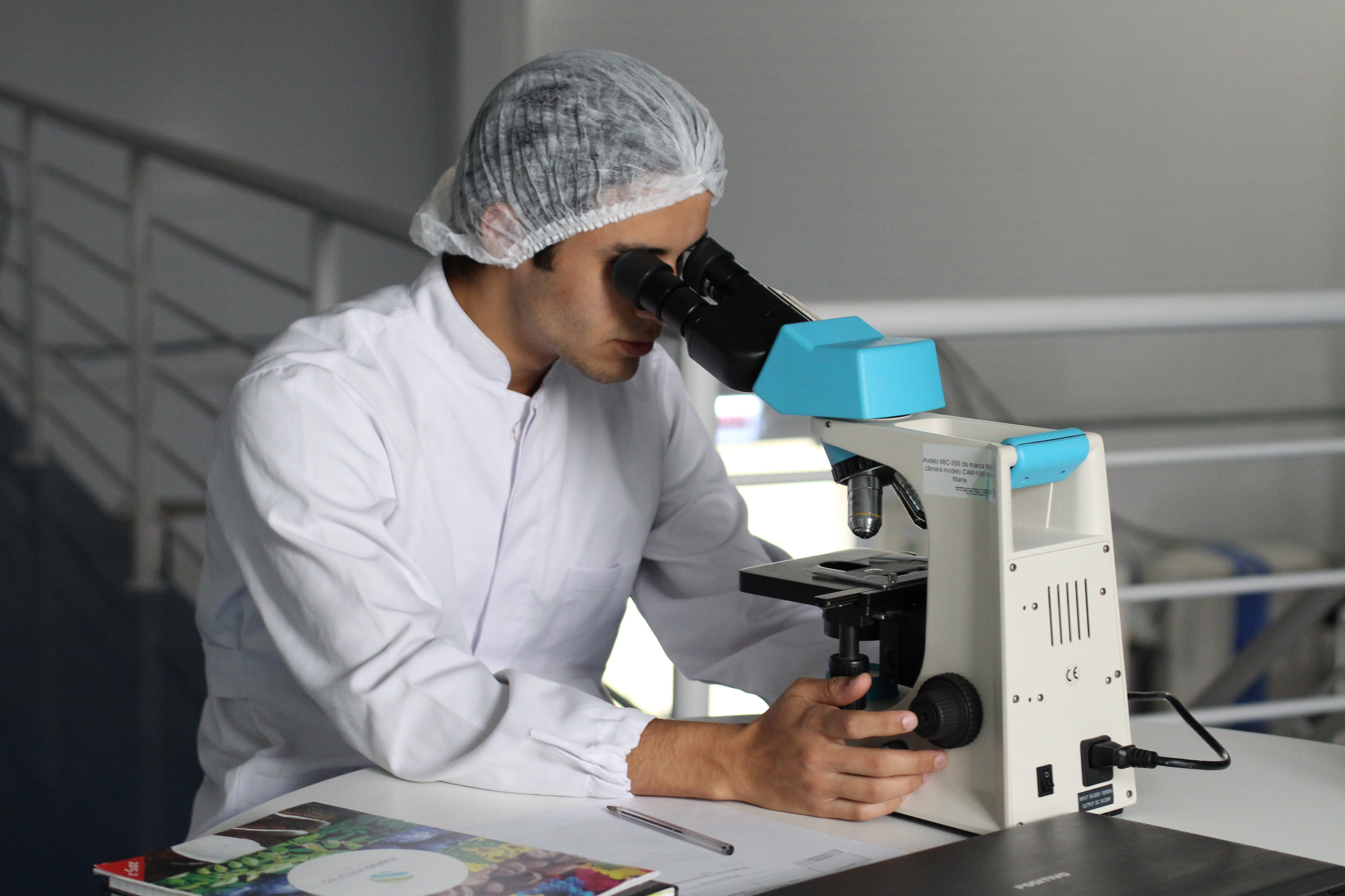 young man waering a hairnet looking at a telescope in a lab