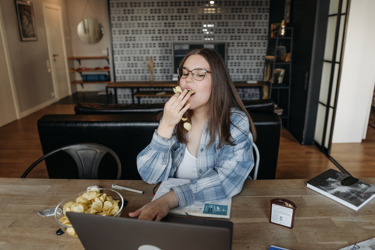 woman eating in front of laptop during virtual meeting