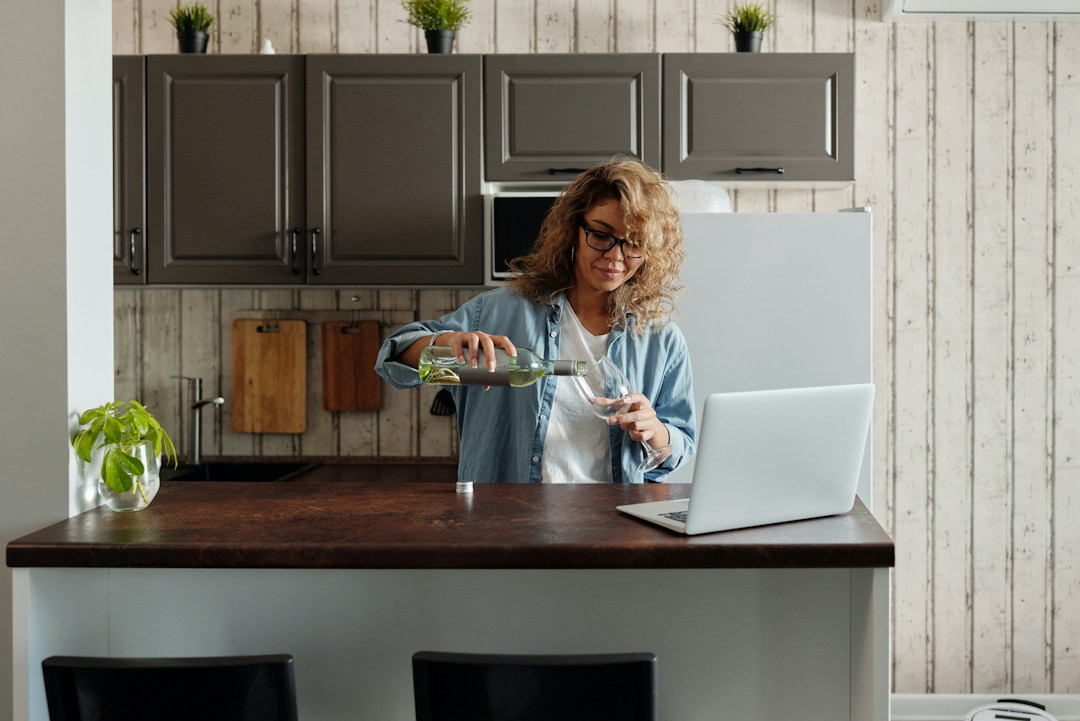 Woman pouring herself a glass of wine over a virtual wine club meeting with her coworkers and team