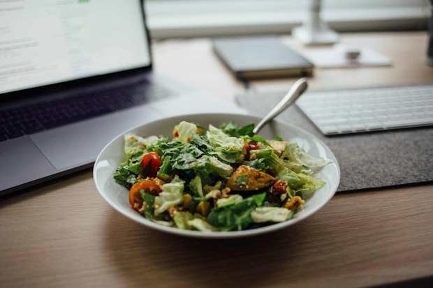 Salat mit Gemüse auf Schreibtisch neben Laptop