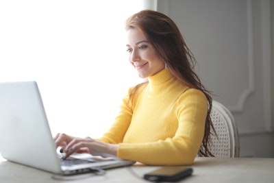 femme souriante travaillant sur ordinateur portable jaune