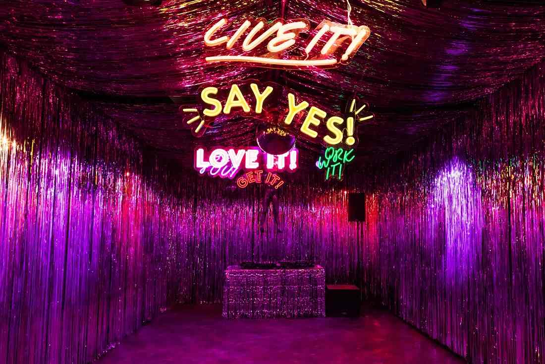A room from the 29 Rooms experiential marketing event that is decorated with tinsel and neon lighting that says “Live it!” and other slogans.