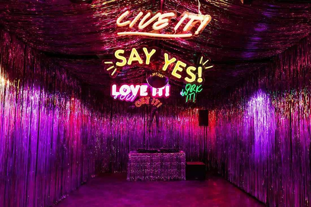 A room from the 29 Rooms experiential marketing event that is decorated with tinsel and neon lighting that says “Live it!” and other slogans.