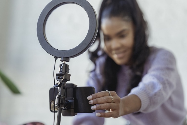 Woman adjusting a phone mounted over a light ring to record herself for a webinar