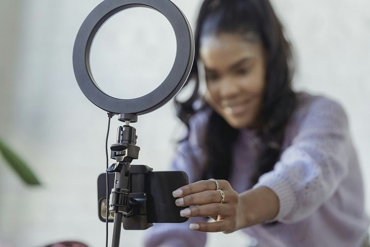 Woman adjusting a phone mounted over a light ring to record herself for a webinar
