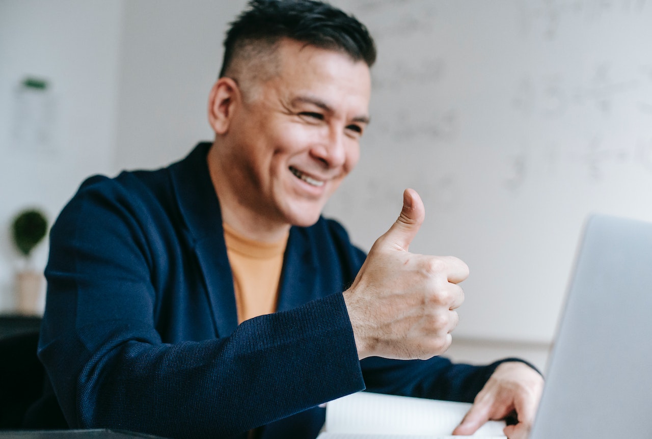 Hombre sonriente con pulgar arriba ante laptop.