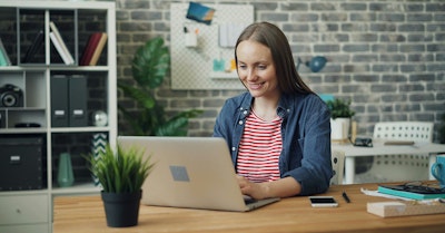 Frau arbeitet lächelnd am Laptop im modernen Büro