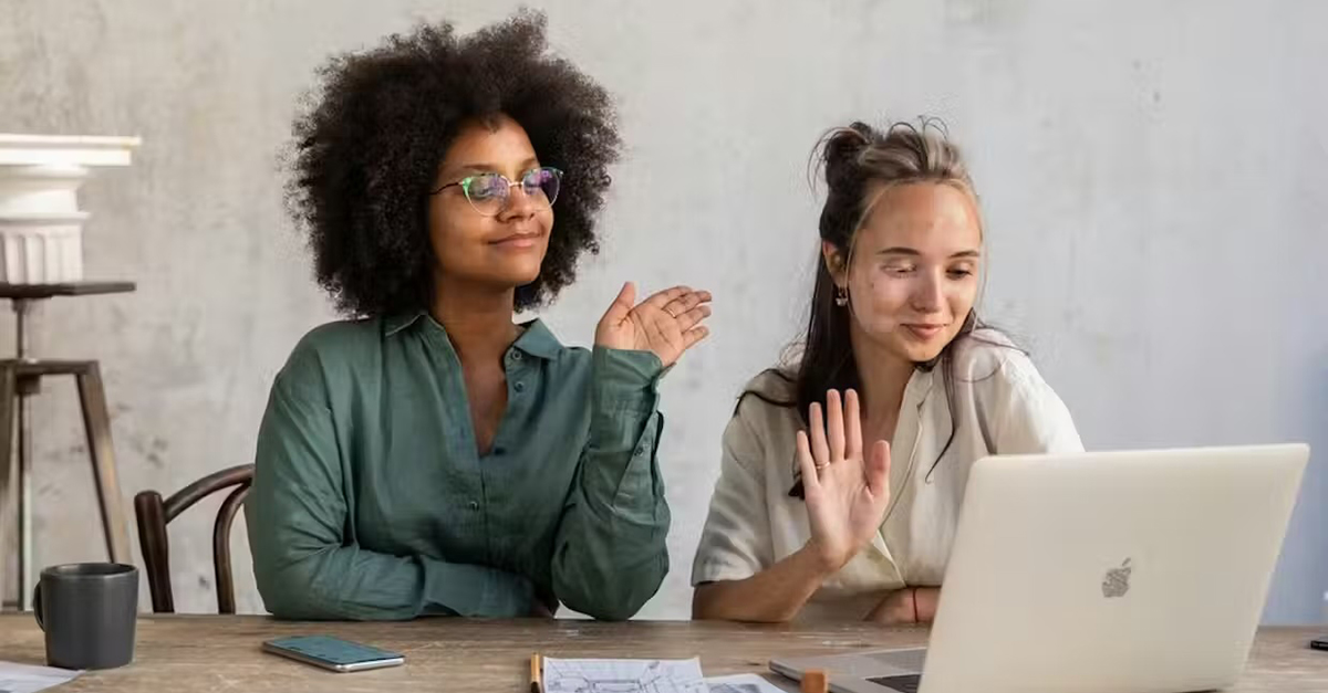 two women sitting next to each other waving at a screen