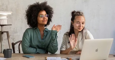 two women sitting next to each other waving at a screen