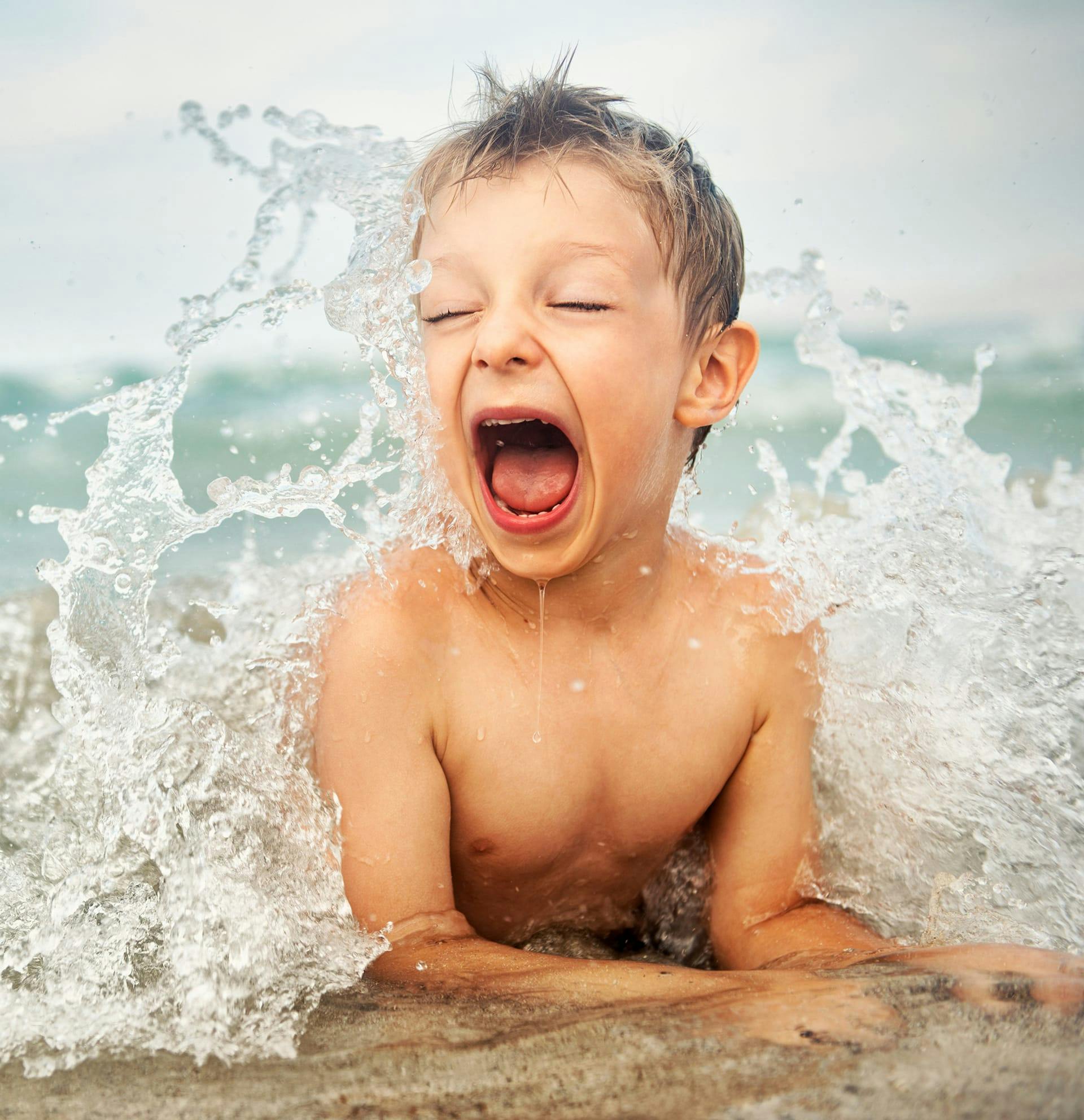 boy laying on beach while small wave crashes on him