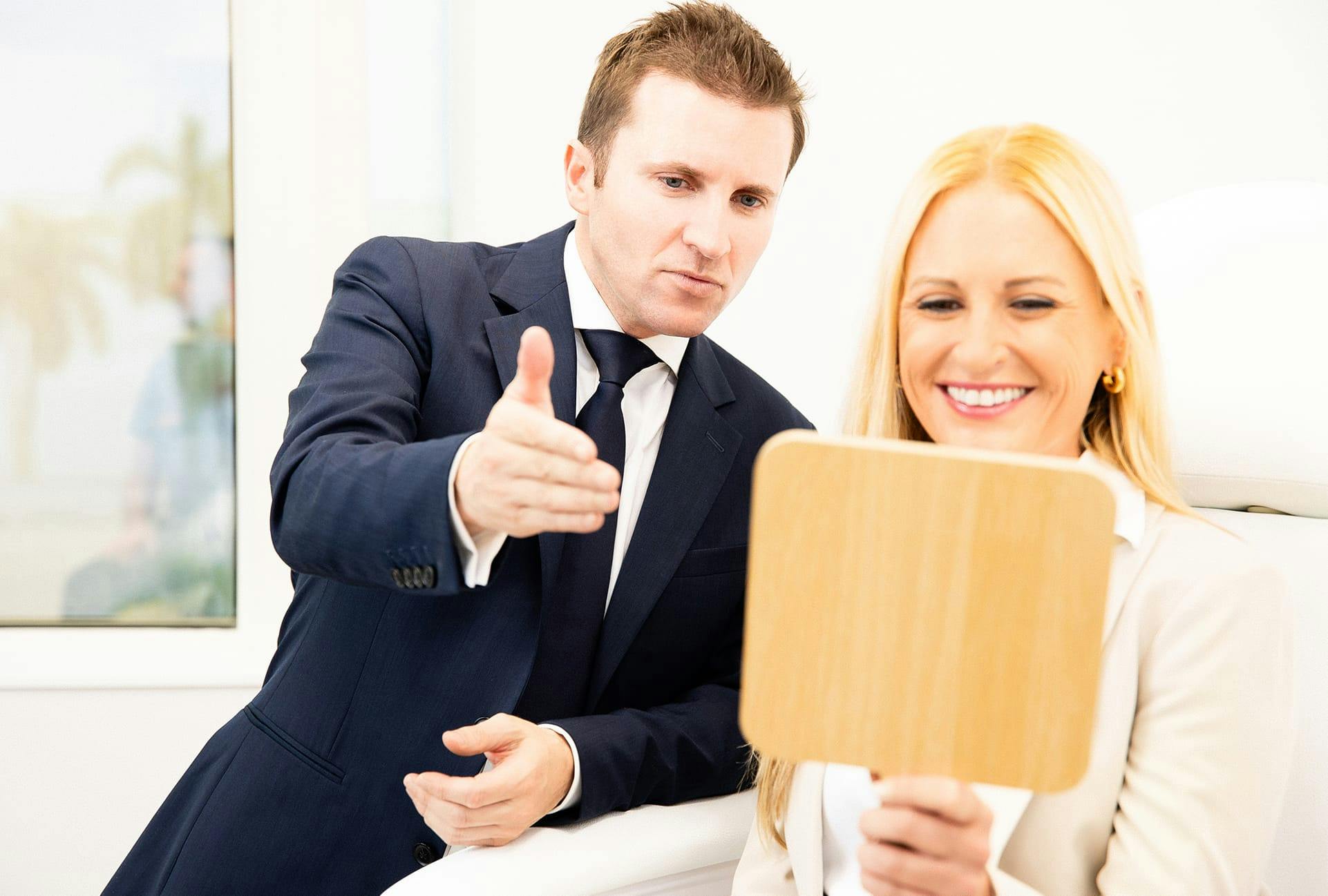 woman looking in hand mirror and doctor pointing at mirror
