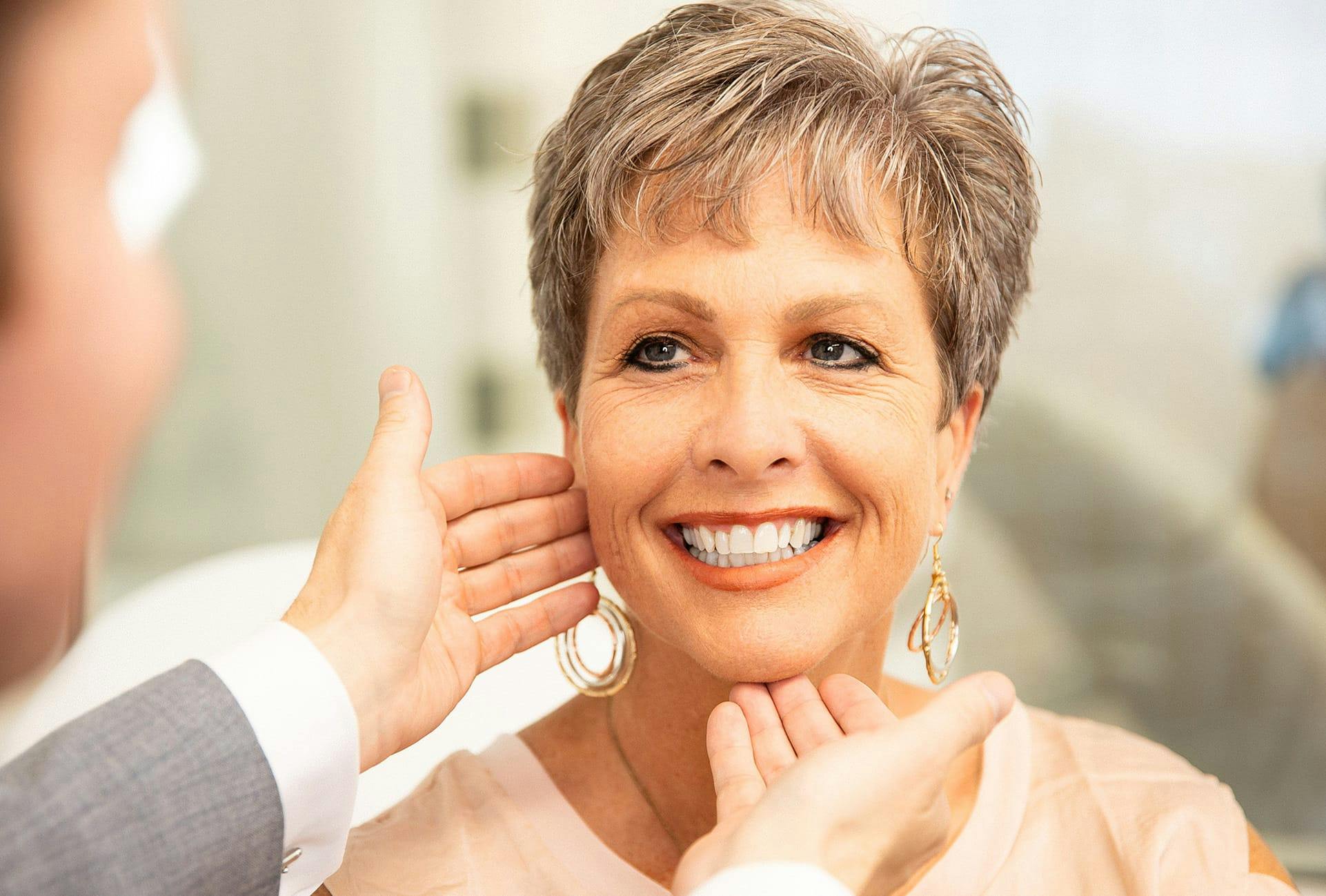 older woman holding up mirror while doctor points at face