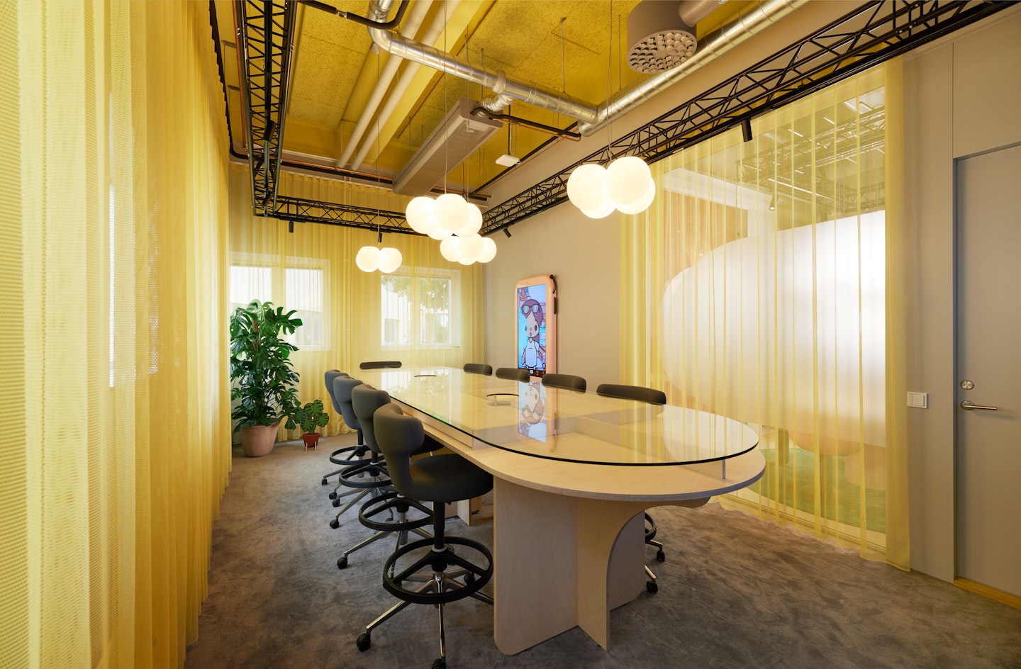 This is an image of a meeting room at Toca Boca Campus. Yellow draping curtains surround the room and with the light shining through them it gives a golden glow. The table has raised glass top.