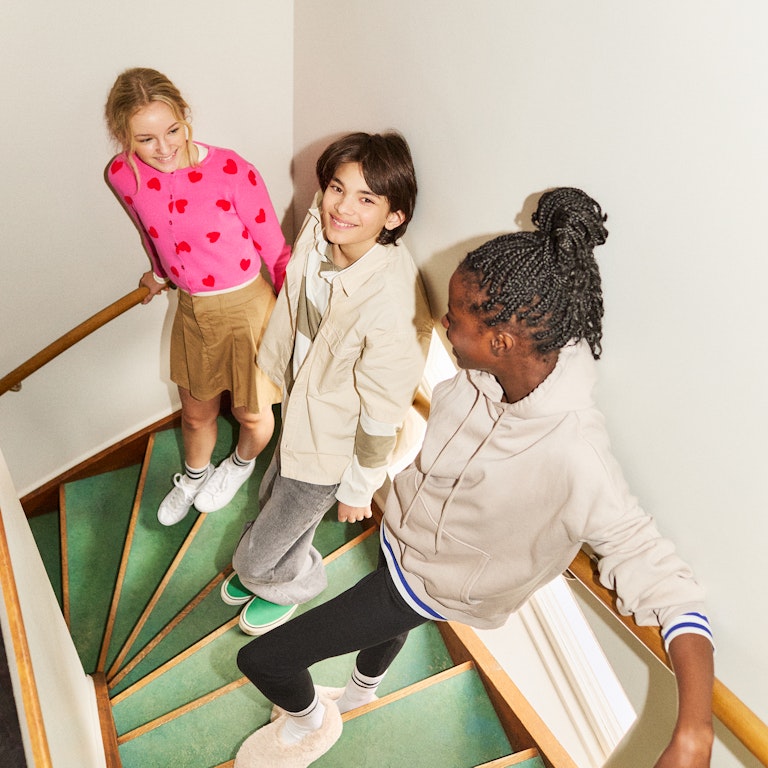 This is an image of a group of tween friends hanging out on a green retro stairwell. They are smiling and seem very comfortable and relaxed with each other.