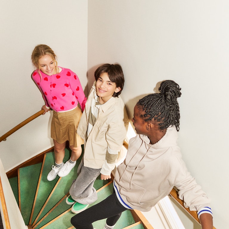 This is an image of a group of tween friends hanging out on a green retro stairwell. They are smiling and seem very comfortable and relaxed with each other.