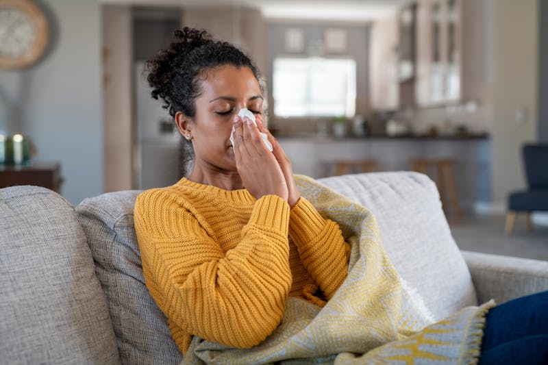 woman blowing nose on couch