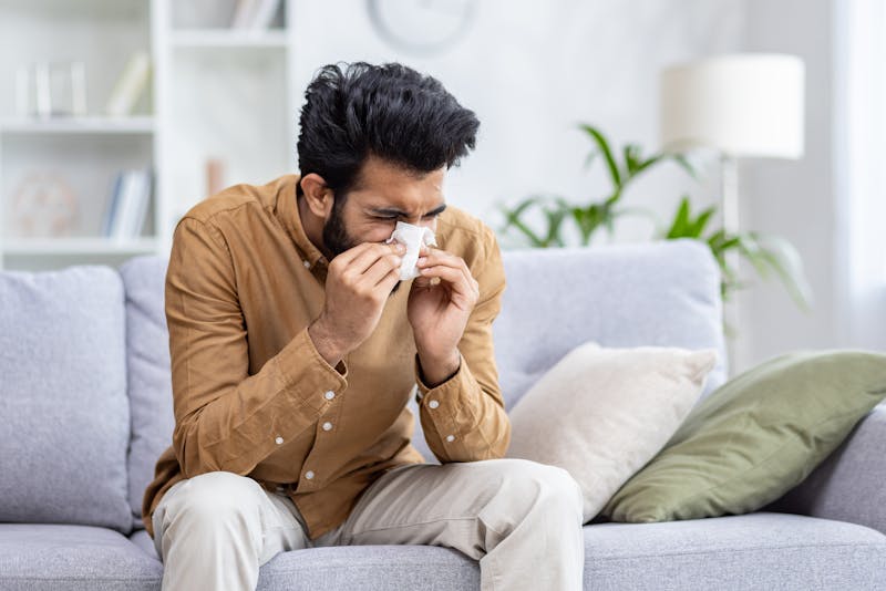 Man sneezing into tissue, may have allergies or sinus infection