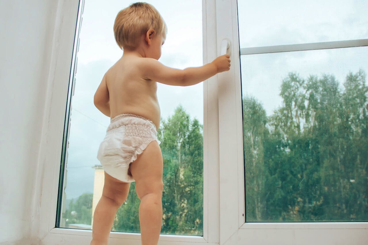 A curious child attempting to open a glass window, emphasizing the importance of childproofing windows for safety.