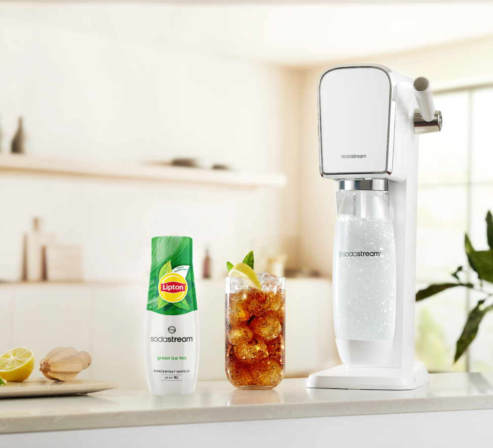 Koncentrat Lipton Green Ice Tea wraz z saturatorem SodaStream i gotowym napojem w szklance stojące na kuchennym blacie.