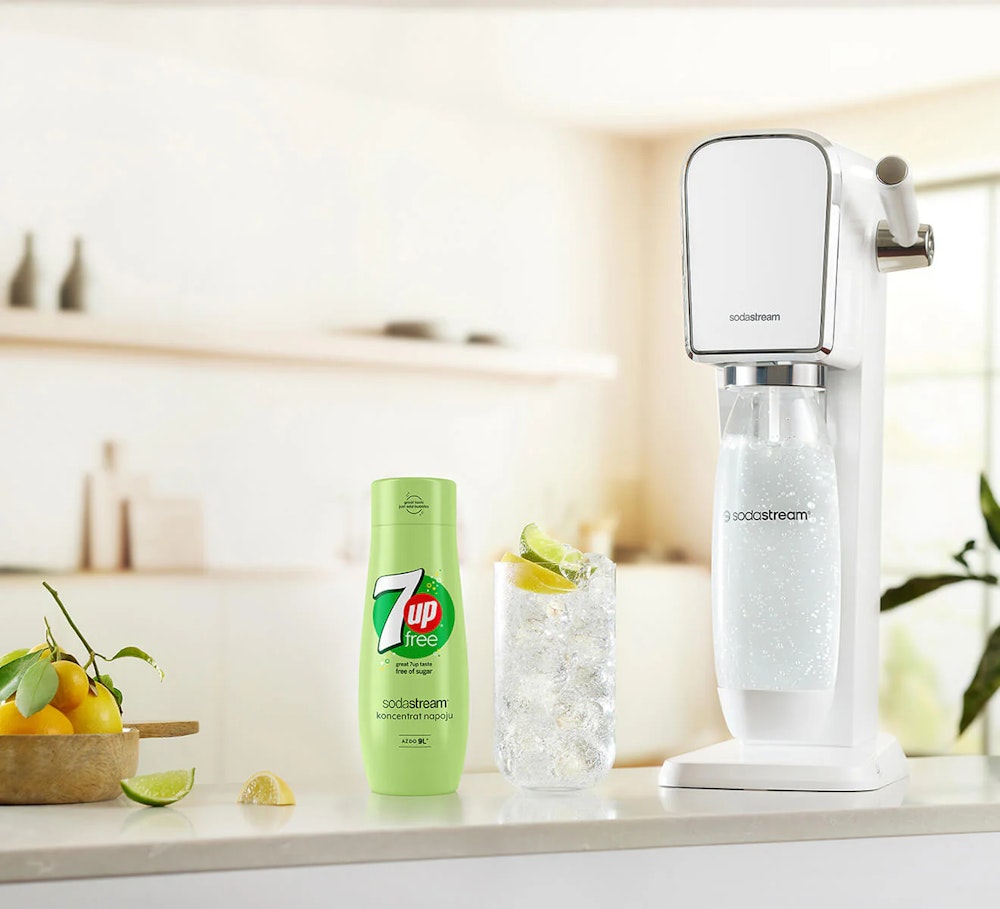Koncentrat 7 UP Zero wraz z saturatorem SodaStream i gotowym napojem w szklance stojące na kuchennym blacie.