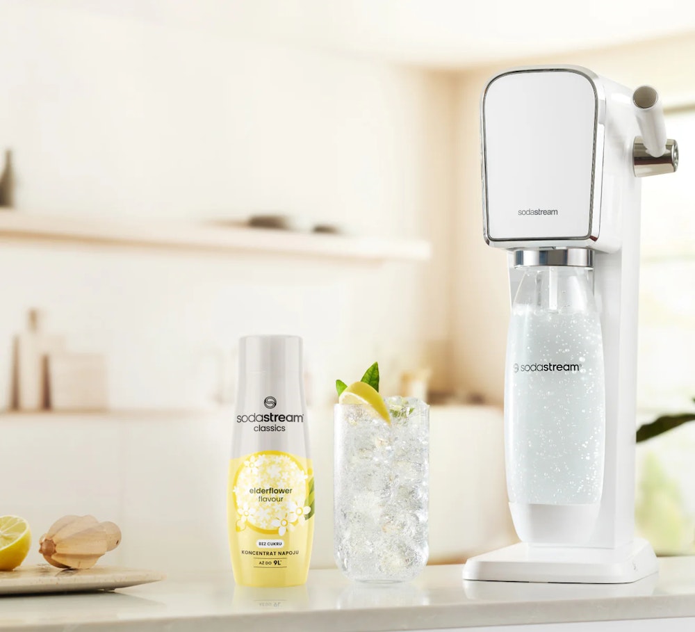 Koncentrat napoju kwiatu czarnego bzu wraz z saturatorem SodaStream i gotowym napojem w szklance stojące na kuchennym blacie.
