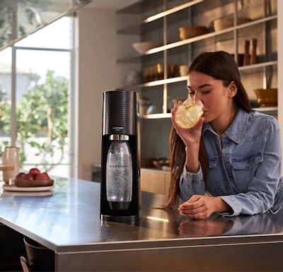 Kobieta pijąca wodę gazowaną z saturatora SodaStream w kuchni