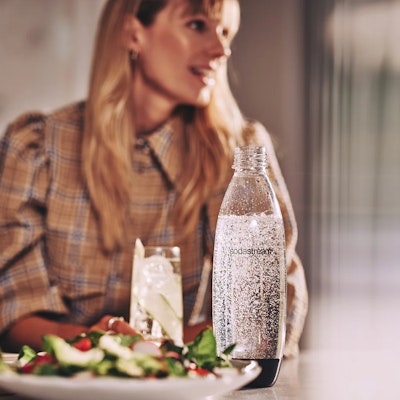 Rozmawiająca przy stole kobieta z butelką SodaStream - tytułowa.