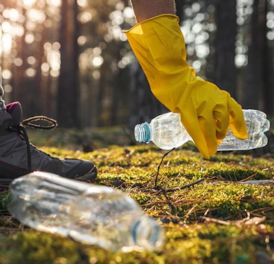 Plastikowe butelki w lesie zbierane przez osobę w żółtych lateksowych rękawiczkach
