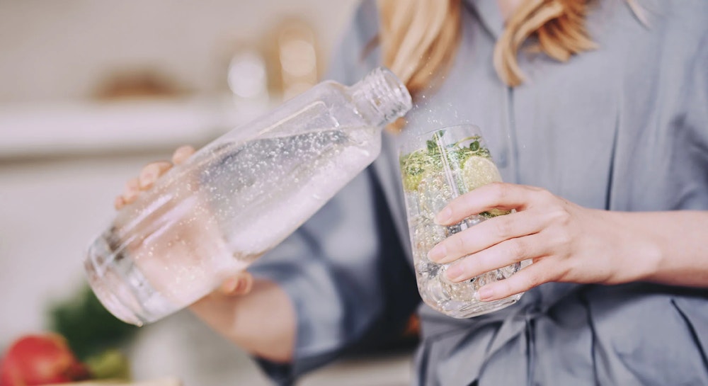 Kobieta nalewa wodę gazowaną z butelki SodaStream do szklanki z limonką