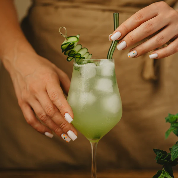 Drink "Elderflower Cucumber Spritz" udekorowany paskiem ogórka zwiniętym w harmonijkę na wykałaczce