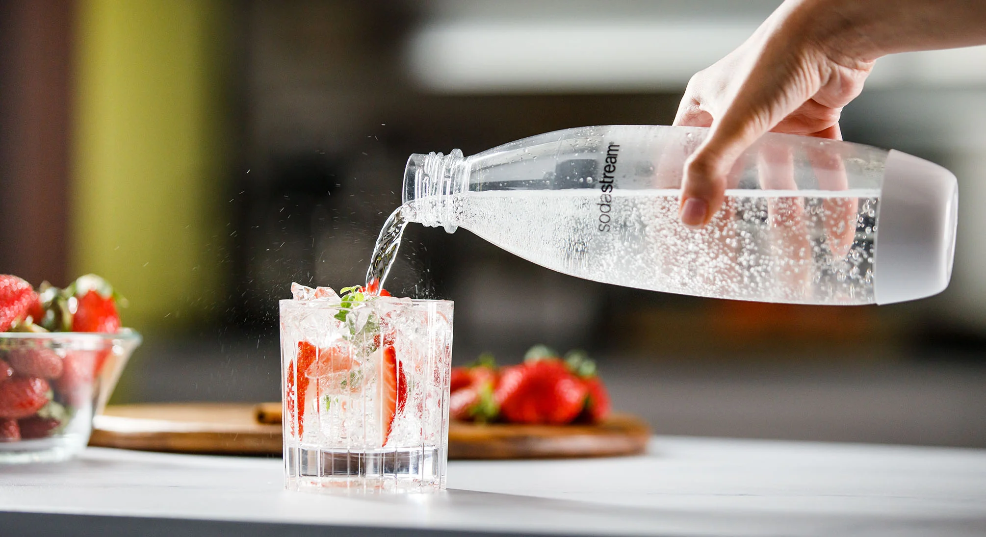 Ręka nalewająca wodę gazowaną z butelki SodaStream do szklanki
