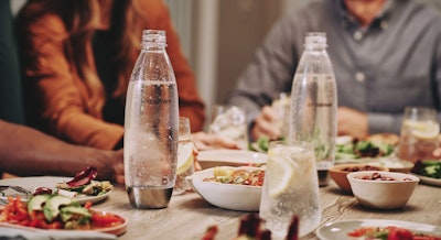 Wielorazowe ekologiczne butelki Sodastream z wodą gazowaną stojące na stole pośród posiłków