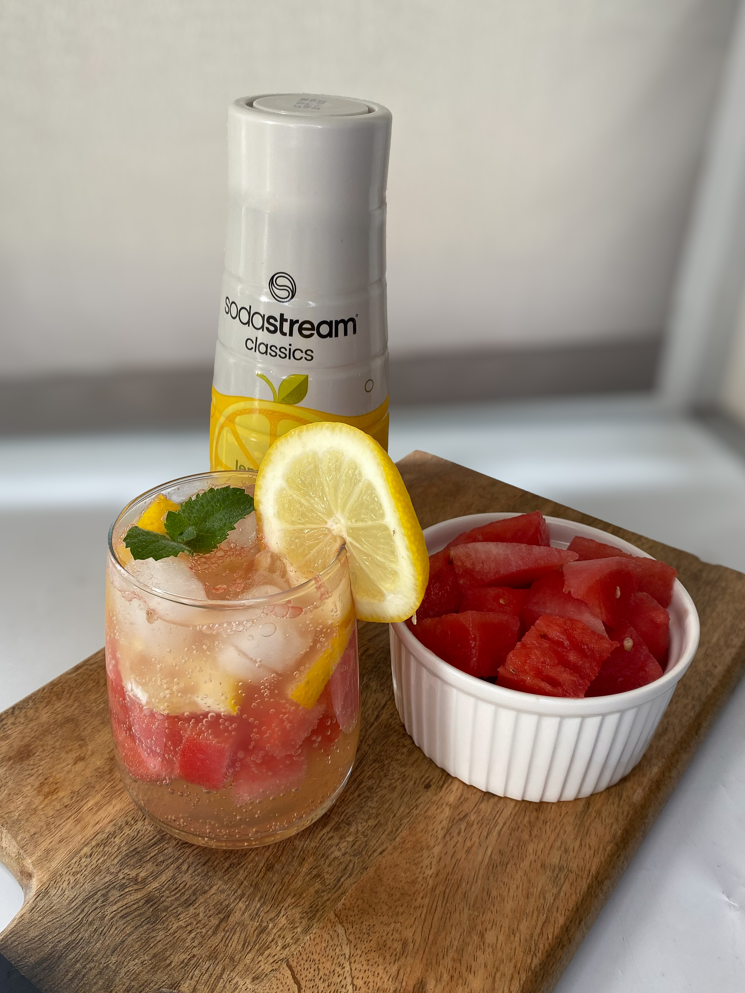 Orzeźwiający drink bezalkoholowy cytryna-arbuz z butelką syropu Lemoniada SodaStream na drewnianej desce do krojenia