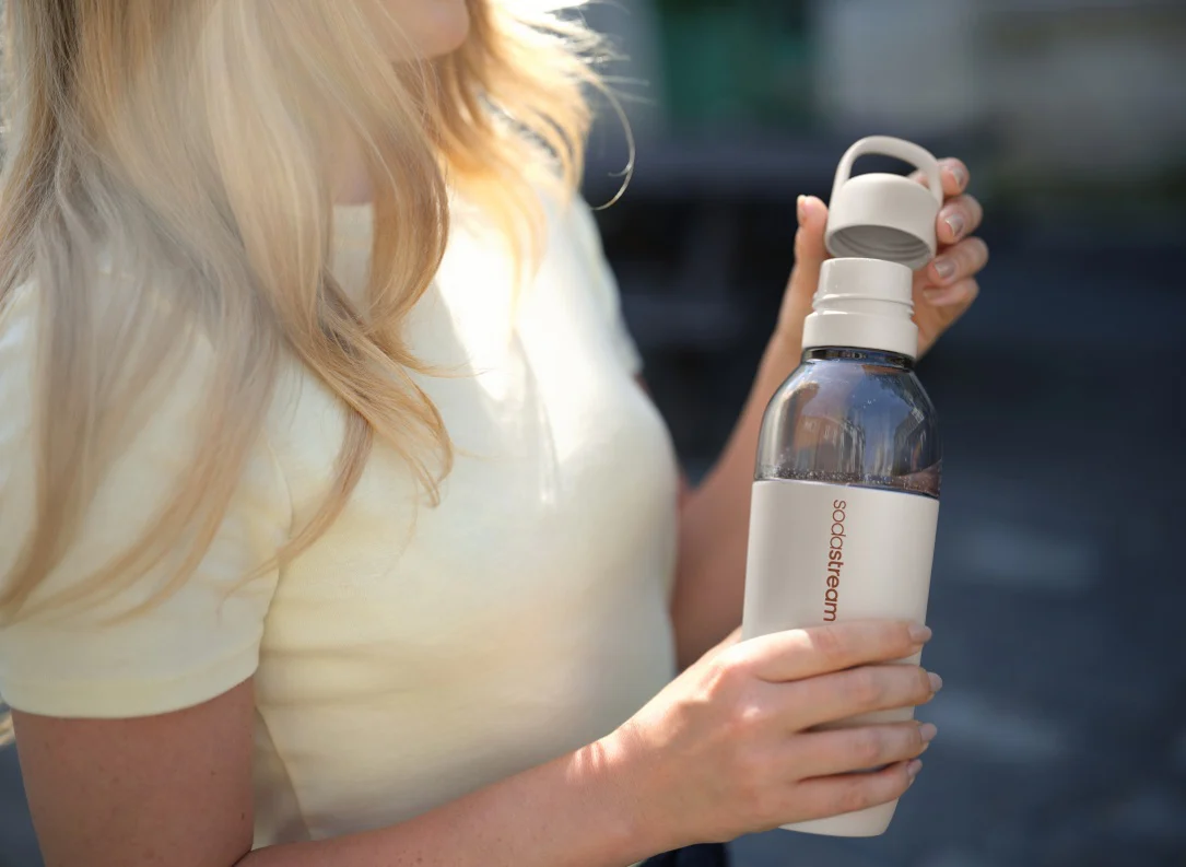 Kobieta pije wodę gazowaną z beżowej butelki SodaStream.