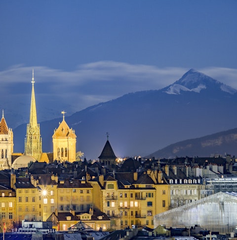 View across Geneva city featuring church and Alps at night