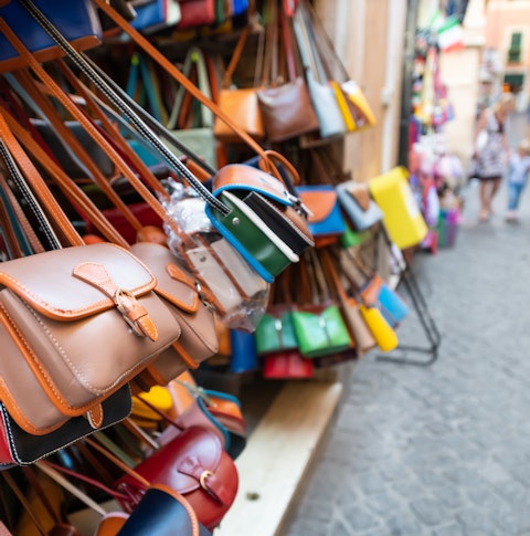 Many leather purse bags in vibrant colours hanging on display in shopping street market in Rome