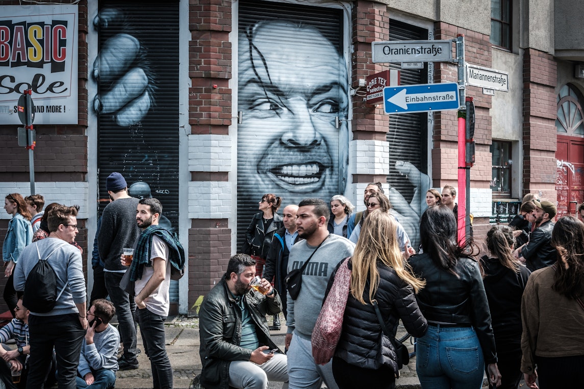 People on a busy street in Kreuzberg, Berlin, with street art in the background
