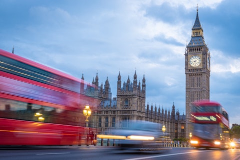 Red busses whirring past London's Big Ben at twilight