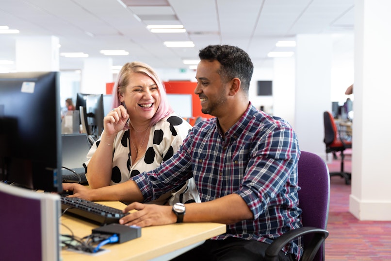 Two people, one male, one female, conversing at a desk with a keyboard