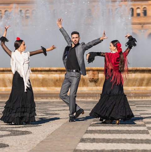 Three people with flamenco outfit dancing in a traditional square