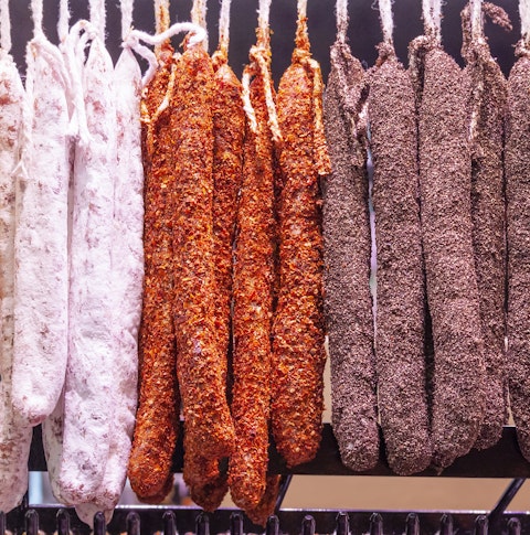 Dried sausages sprinkled with different colors of spices are hung in a row on a hanger