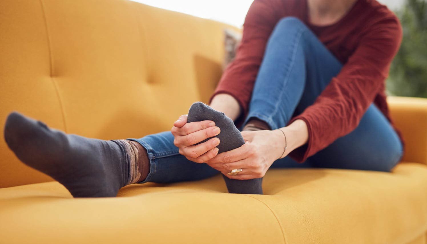 woman sitting on a couch holding her foot in pain