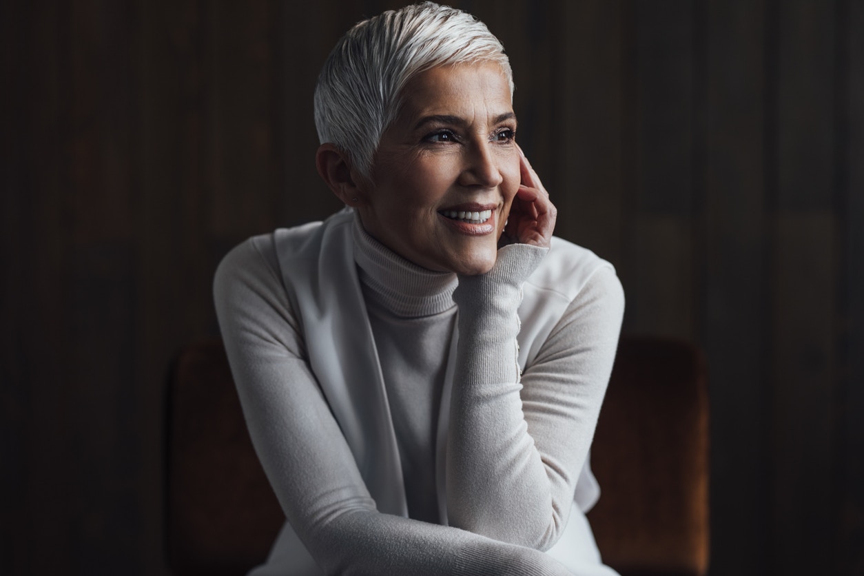 Woman in her 60s smiles looking away from camera to highlight her defined jawline to emulate the potential results of a facelift in Beverly HIlls with Dr. Torkian
